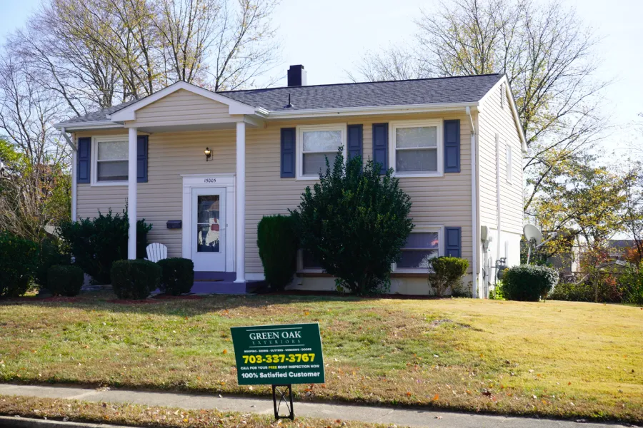 A two-story beige house with blue shutters and a white front door displays a 'Green Oak Exteriors' sign in the yard.