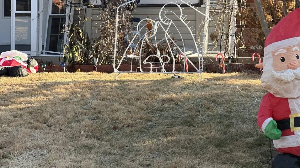 Christmas nativity scene, two candy canes, and an inflatable Santa Claus on a dry grass lawn.